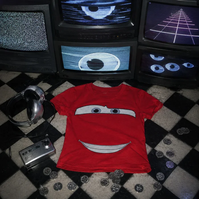 Red graphic T-shirt beneath vintage television screens with arcade tokens.