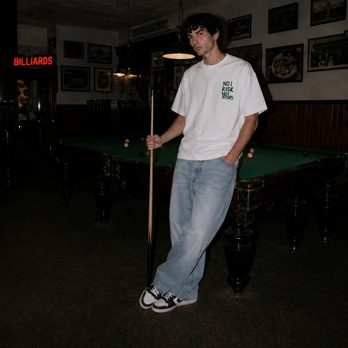 Man in a white T-shirt standing beside a pool table.