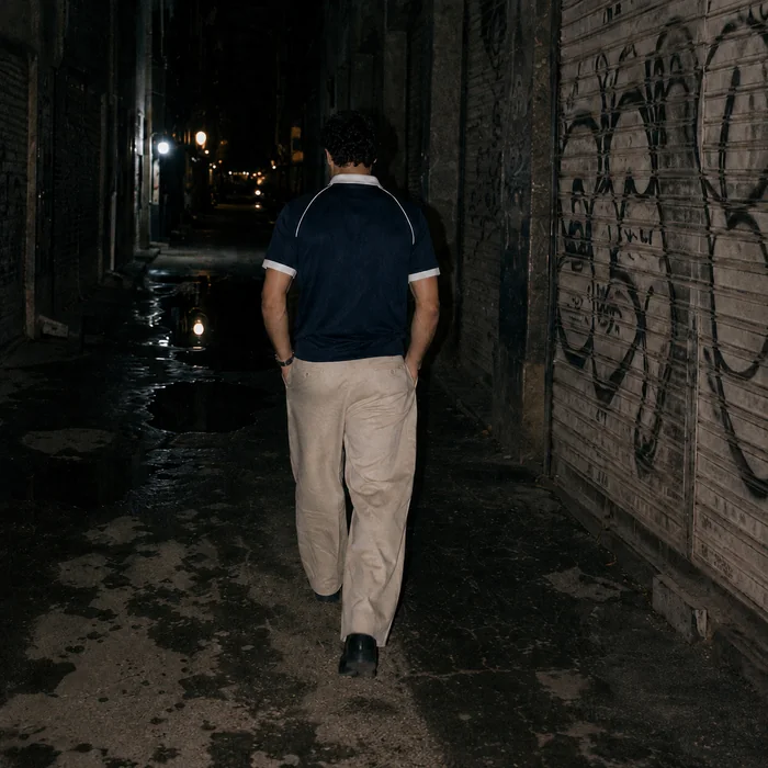 Man in a navy collared shirt walking away along an alley.