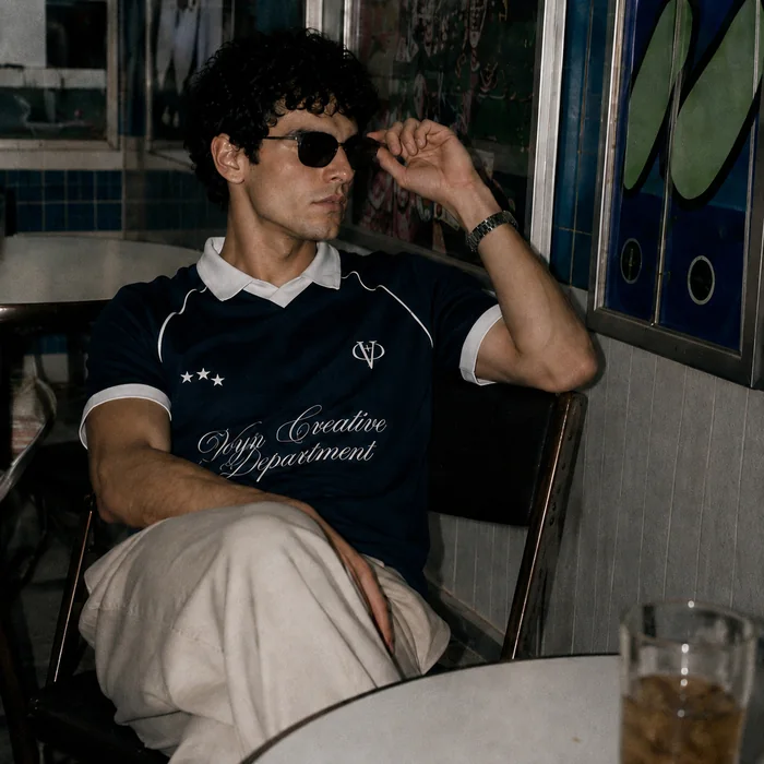 Man in a navy collared shirt seated outside a cafe.