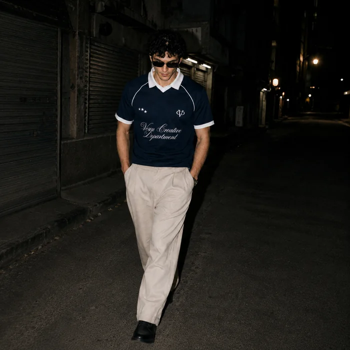 Man in a navy collared shirt walking toward the camera at night.