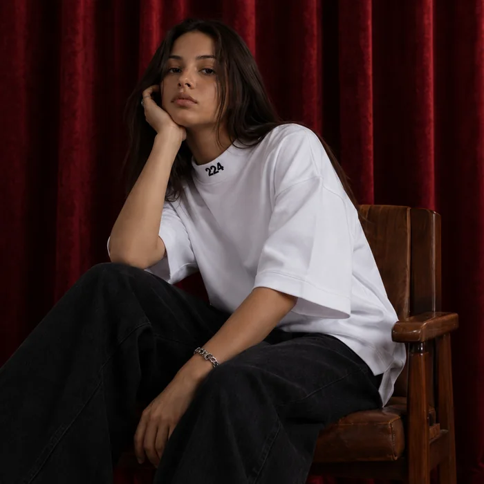 Woman in a white T-shirt seated in front of a red curtain.