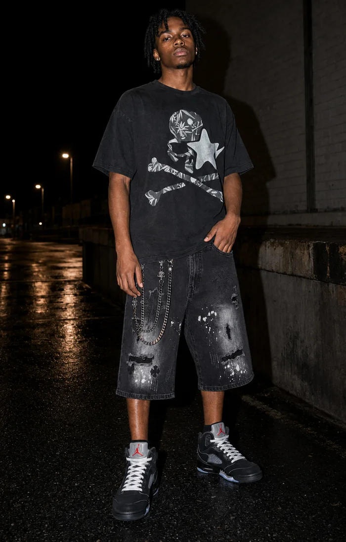 Man in a black graphic T-shirt and denim shorts at night.