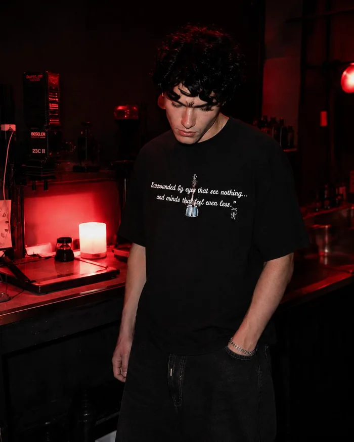 Man in a black printed T-shirt looking down in a red-lit room.