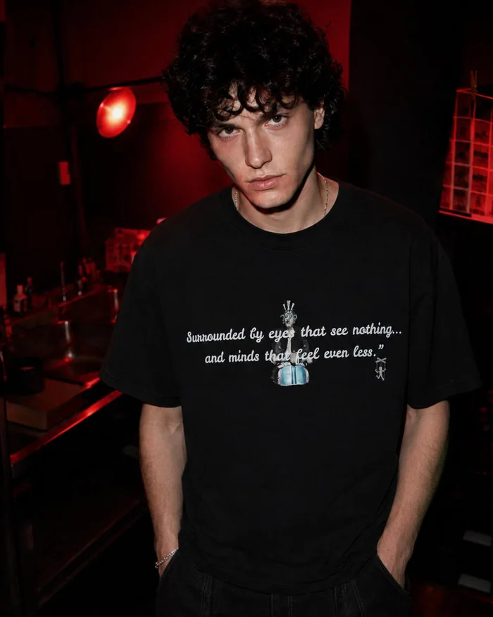 Front portrait of a man in a black printed T-shirt in a red-lit room.