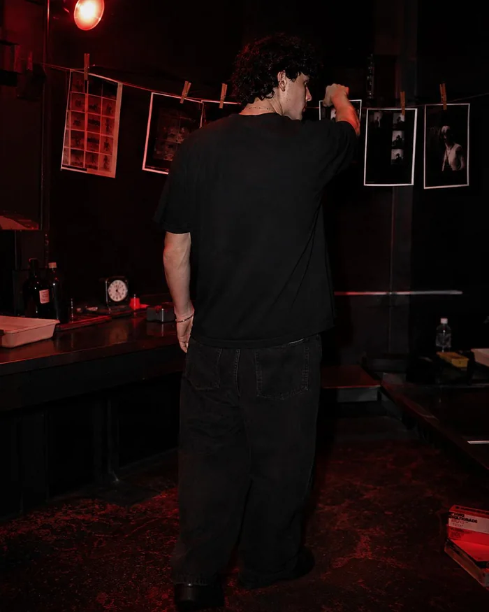 Back view of a man in a black printed T-shirt in a red-lit room.