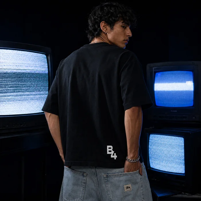 Back view of a black T-shirt against blue television screens.